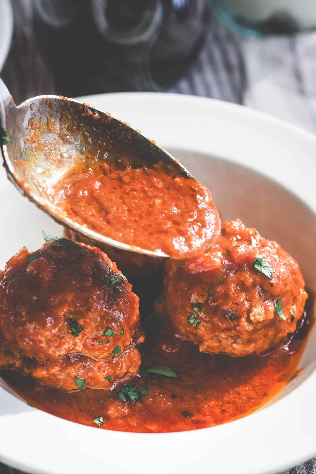 Spooning marinara sauce onto soft ricotta meatballs, Italian style.