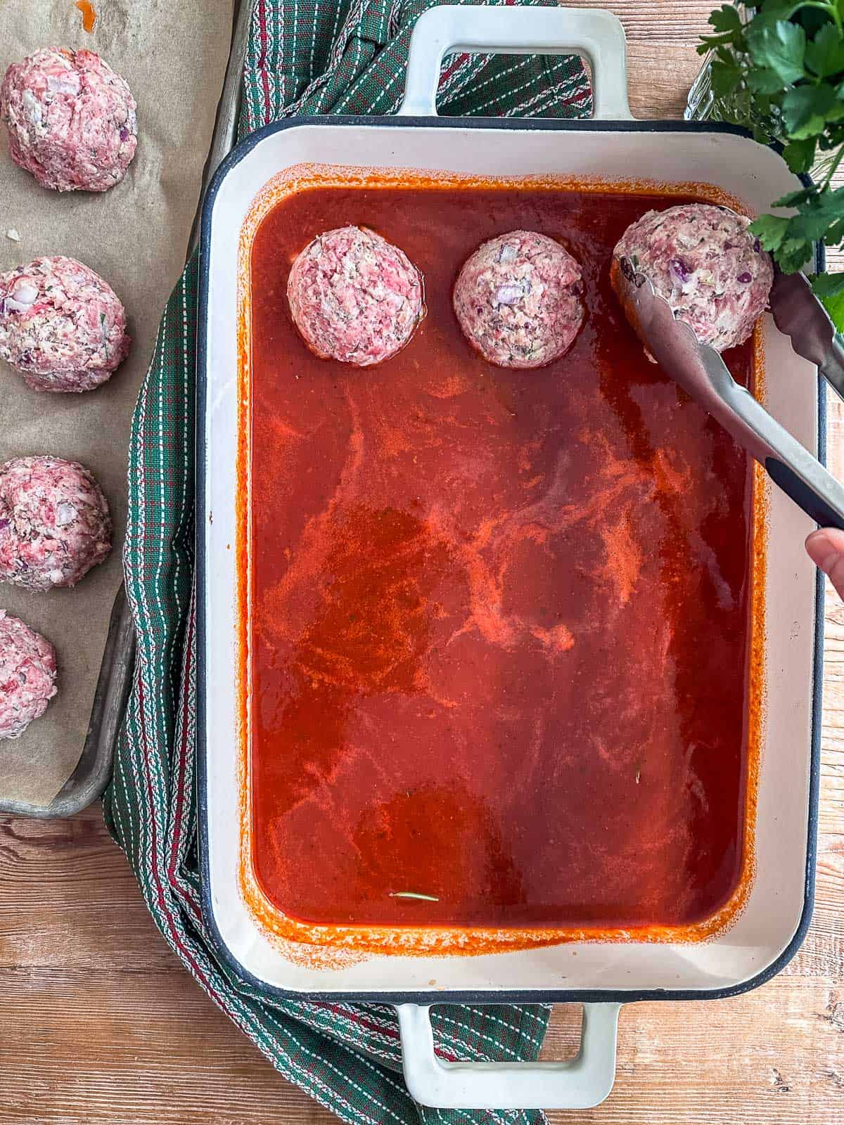 Adding ricotta meatballs to marinara sauce before baking.