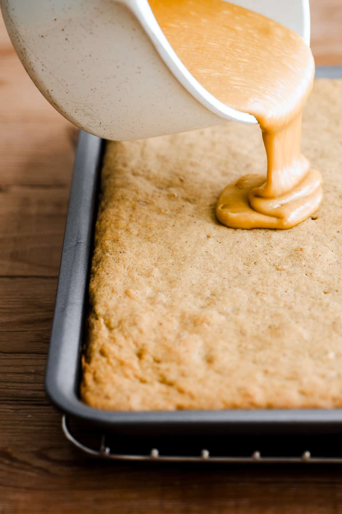 Pouring cooked fudge frosting onto coffee fudge traybake.