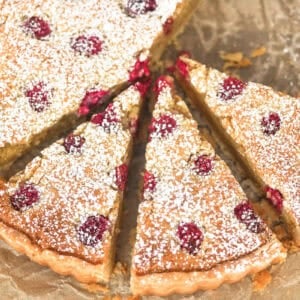 A raspberry frangipane tart topped with powdered sugar, sliced into wedges.