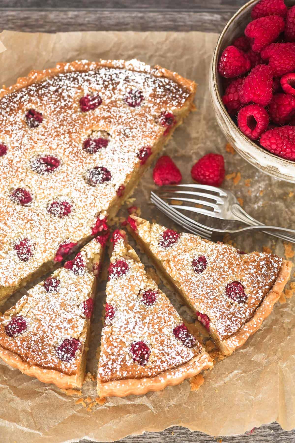 Raspberry frangipane tart, sliced, on parchment paper.