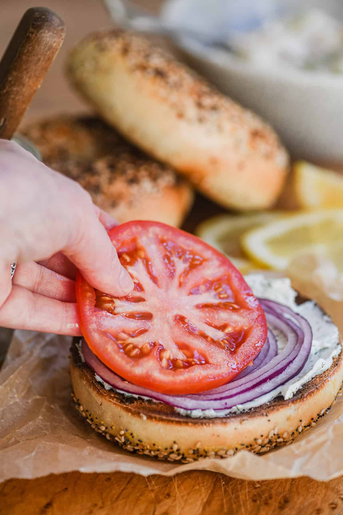 Adding a slice of tomato to a whitefish salad topped bagel.