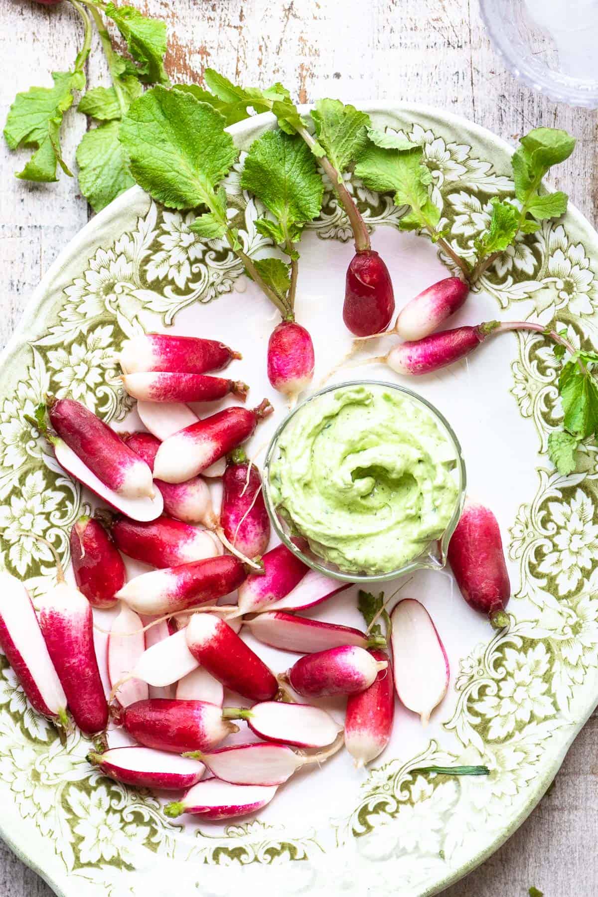 French breakfast radishes with a small bowl of tarragon butter on a green floral plate.