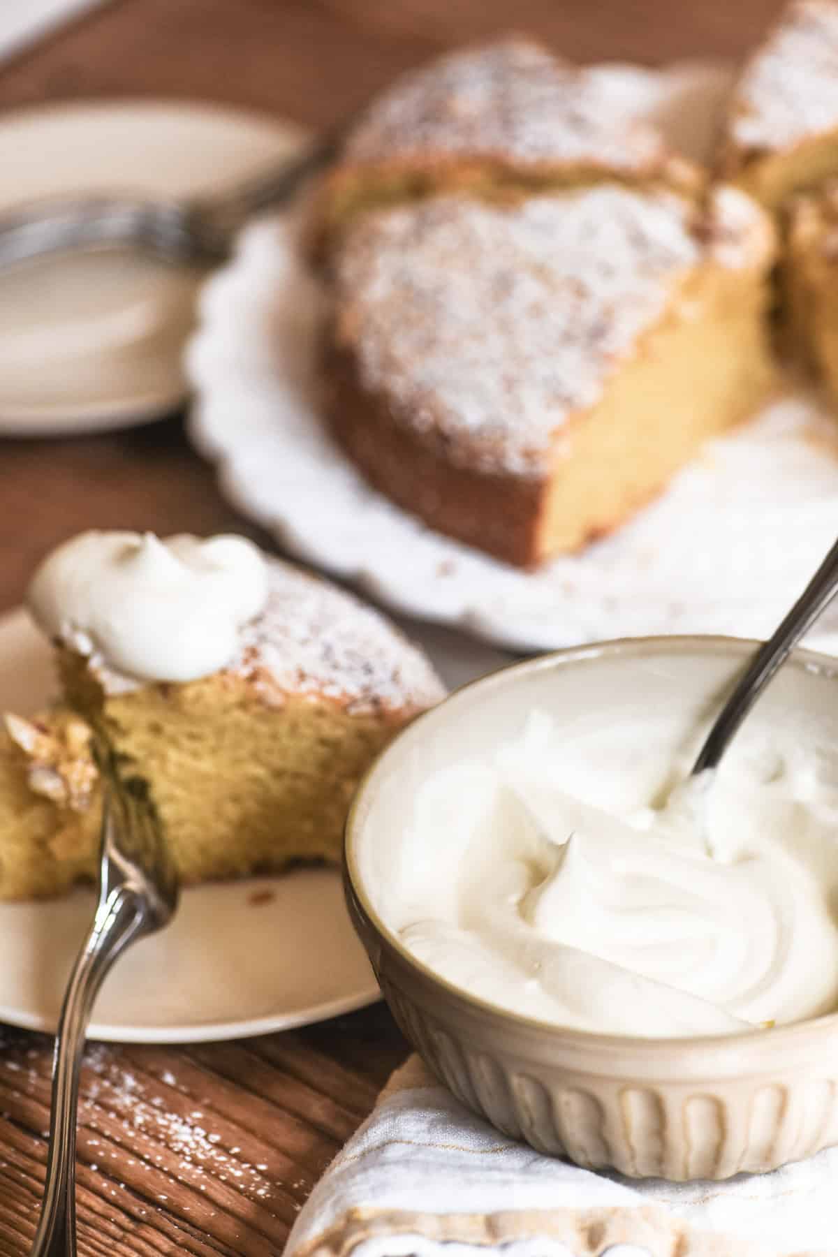 almond olive oil cake with a small bowl of whipped cream.