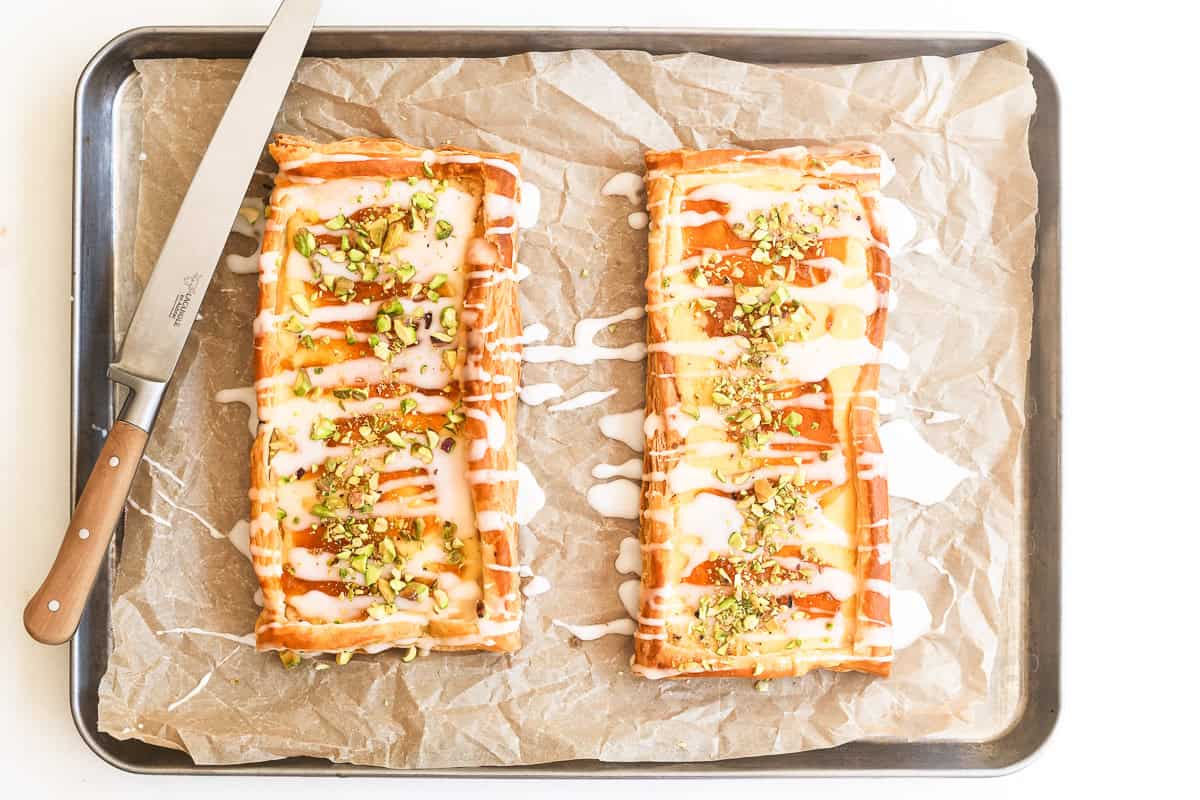 two puff pastry danish with apricot and pistachio on a sheet pan.