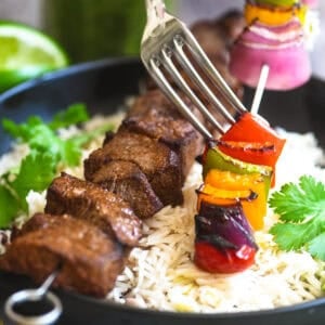 Fork pushing veggies off a fajita skewer.