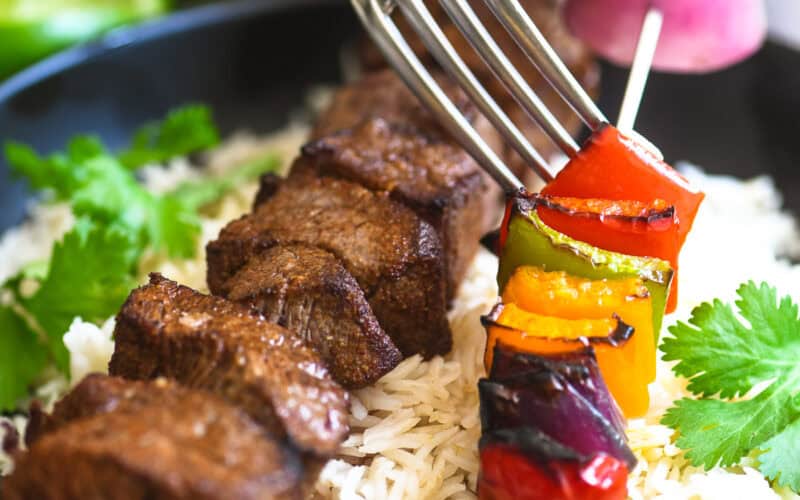 Fork pushing veggies off a fajita skewer.