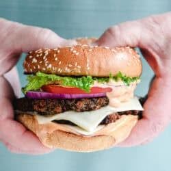 Man's hands holding a veggie smash burger with all the fixings.