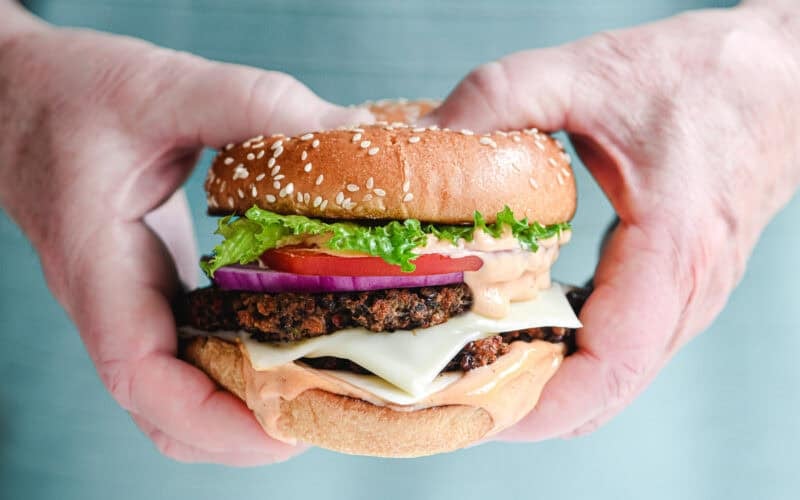 Man's hands holding a veggie smash burger with all the fixings.