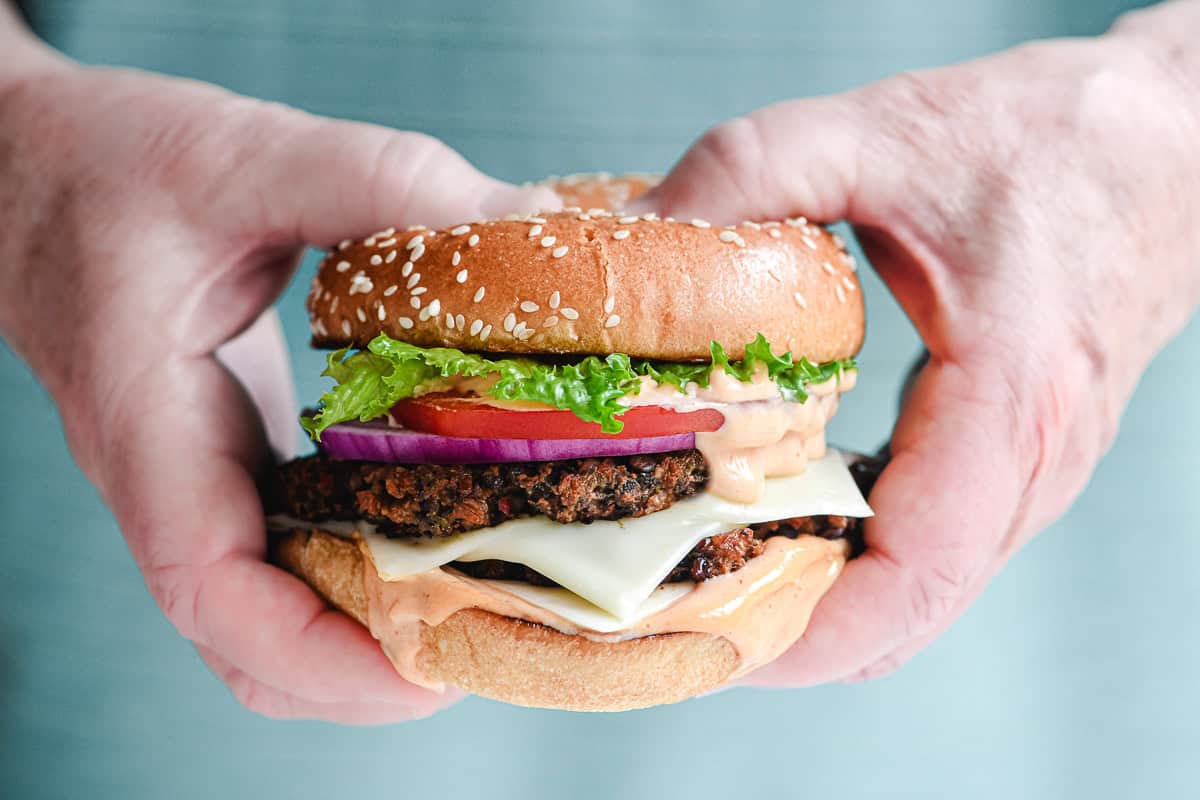 Man's hands holding a veggie smash burger with all the fixings.