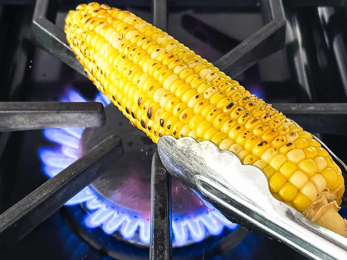 Roasting corn on the cob over an open gas flame, with tongs.