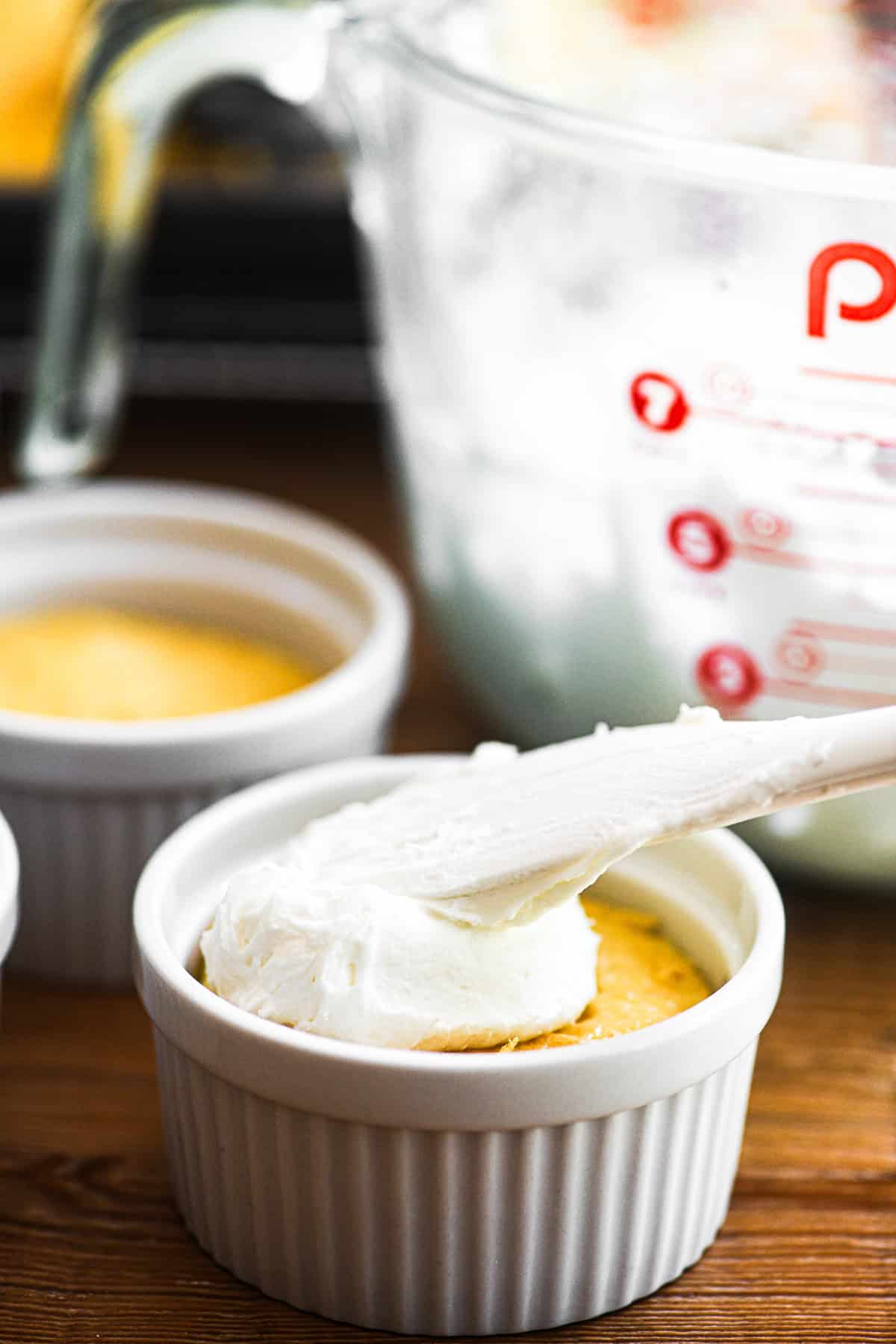 Spreading lemon frosting over lemon cake in a ramekin for lemon dot cake.
