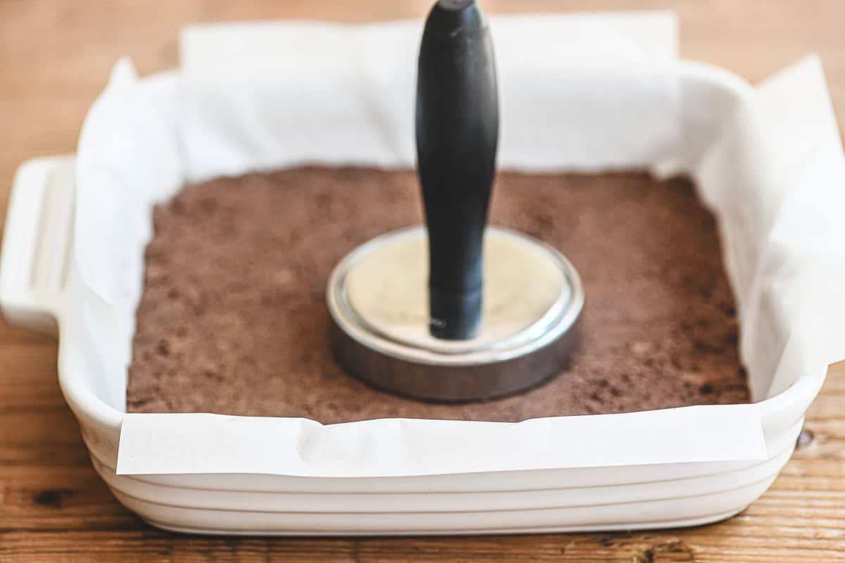 tamping down chocolate shortbread crust in a 9x9 pan for black bottom lemon bars.