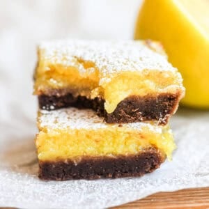 Bright yellow black bottom lemon bars, stacked, with bite taken.