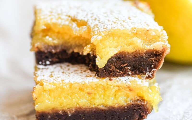Bright yellow black bottom lemon bars, stacked, with bite taken.