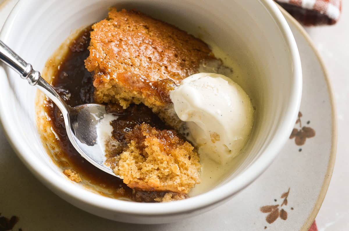 A bowl of butterscotch pudding cake and ice cream, with spoon.
