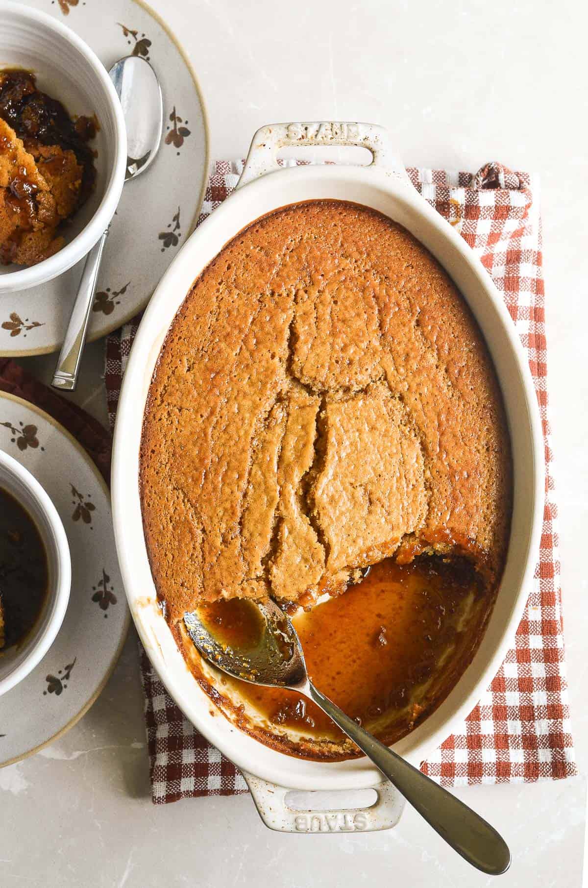Butterscotch pudding cake in an oval baker, scooped out with sauce in the bottom of the pan.