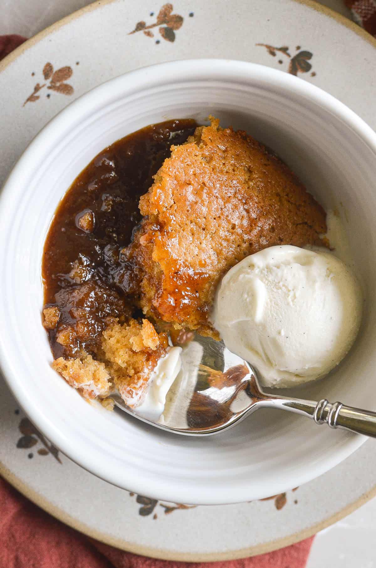 A serving of butterscotch pudding cake in a bowl with vanilla ice cream.