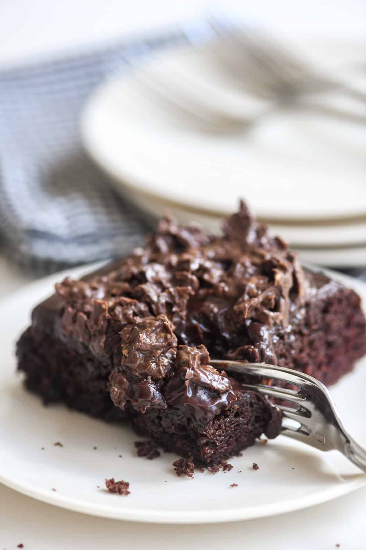 Taking a bite of a piece of chocolate crunch cake, on a small white plate.