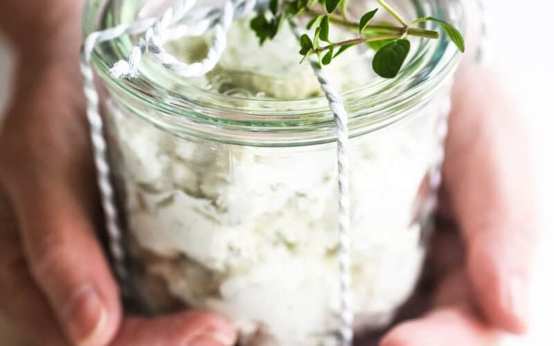 Holding a small jar of homemade Boursin style cheese tied with a ribbon for gifting.