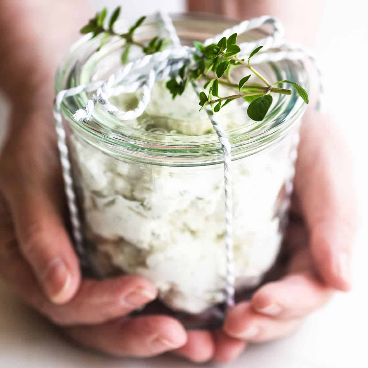 Holding a small jar of homemade Boursin style cheese tied with a ribbon for gifting.