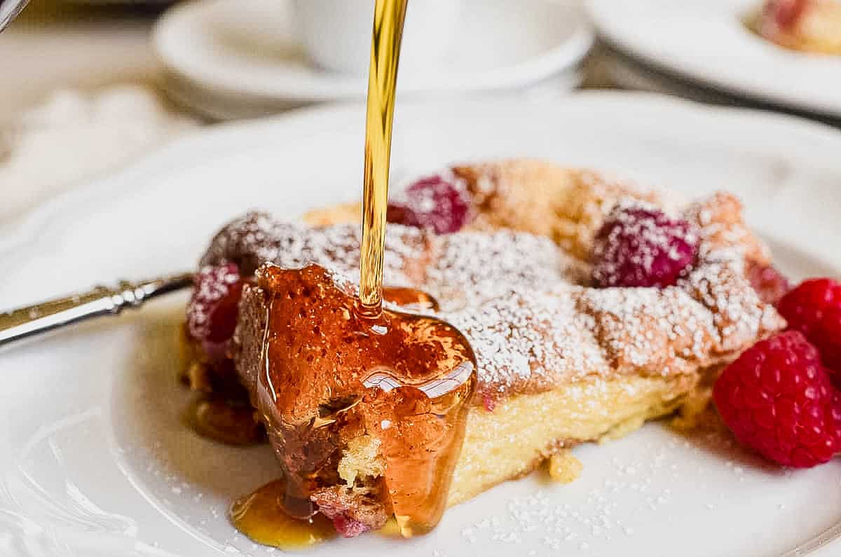 Pouring syrup on a plate of raspberry baked French toast.