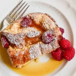 A piece of raspberry baked French toast on a plate with syrup and fresh raspberries.