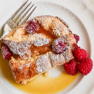 A piece of raspberry baked French toast on a plate with syrup and fresh raspberries.