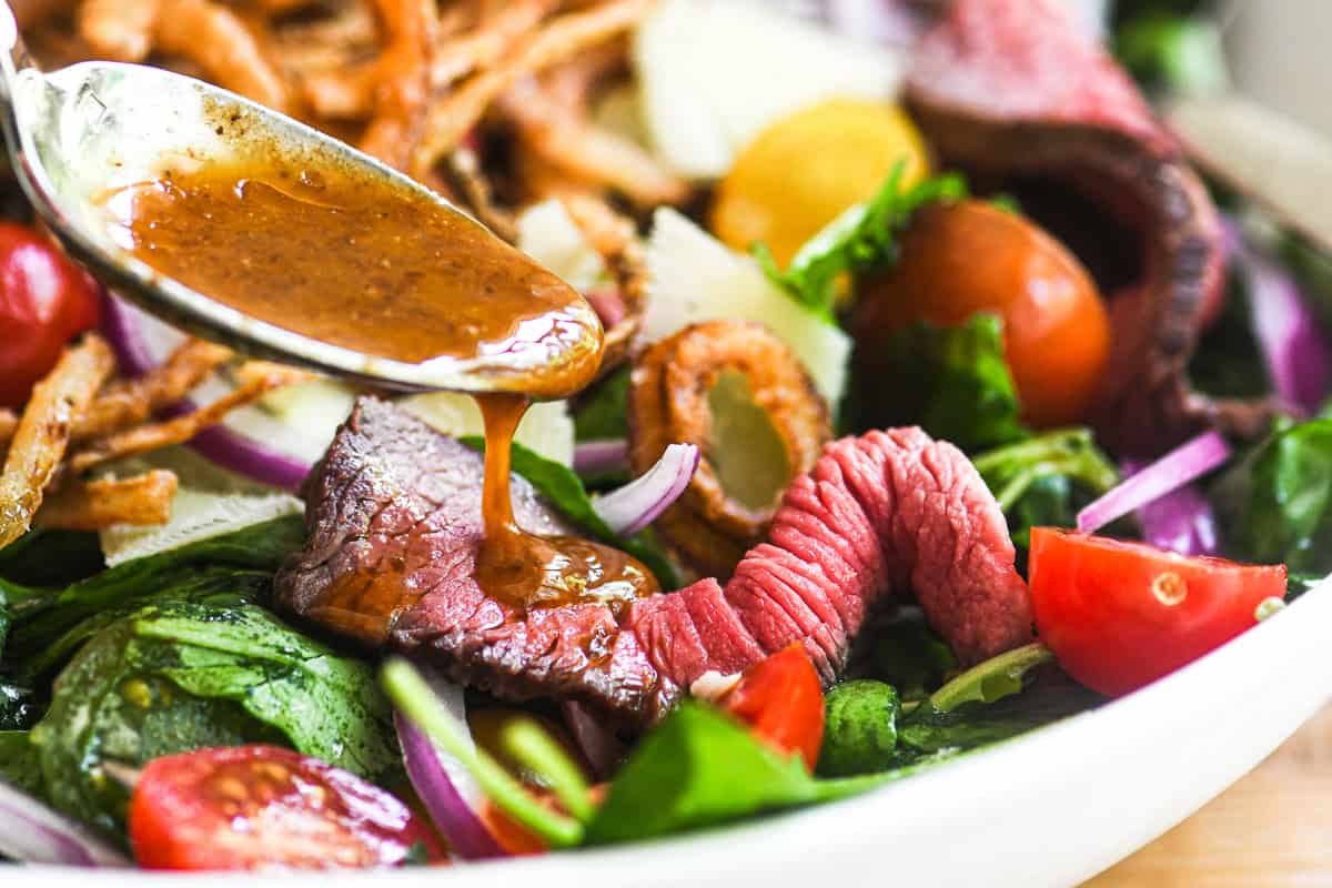 Spooning A1 vinaigrette dressing onto a steak salad.