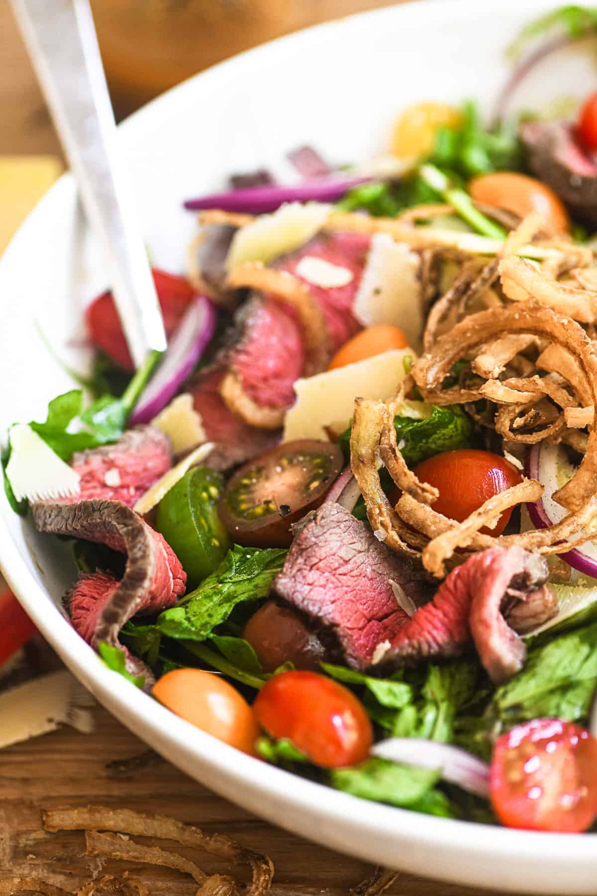 Steak salad in a white serving bowl with onions rings.