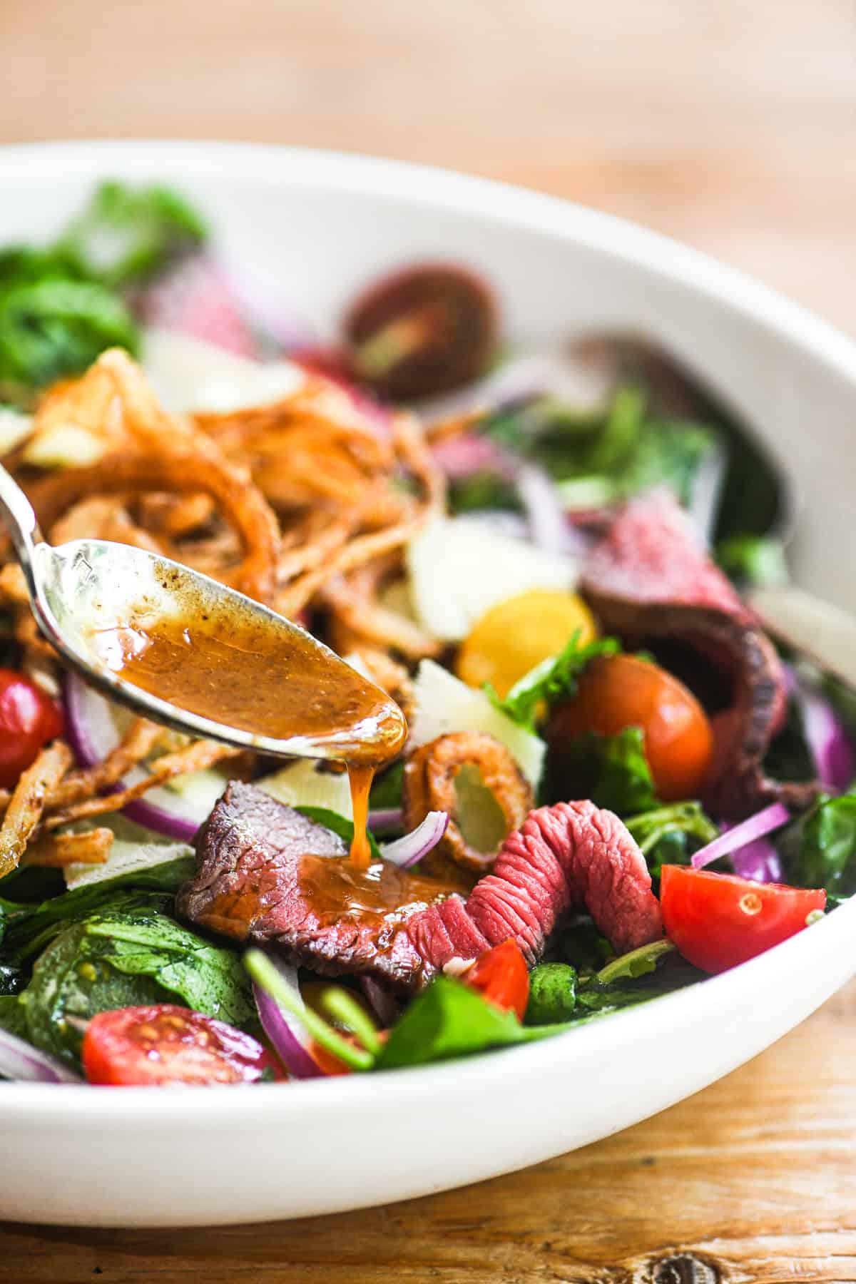 Spooning A1 vinaigrette onto a steak salad.