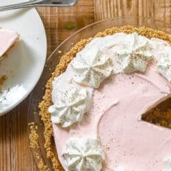 Frozen Pink Squirrel Pie topped with whipped cream, with piece on a plate.