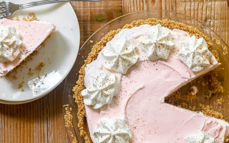 Frozen Pink Squirrel Pie topped with whipped cream, with piece on a plate.