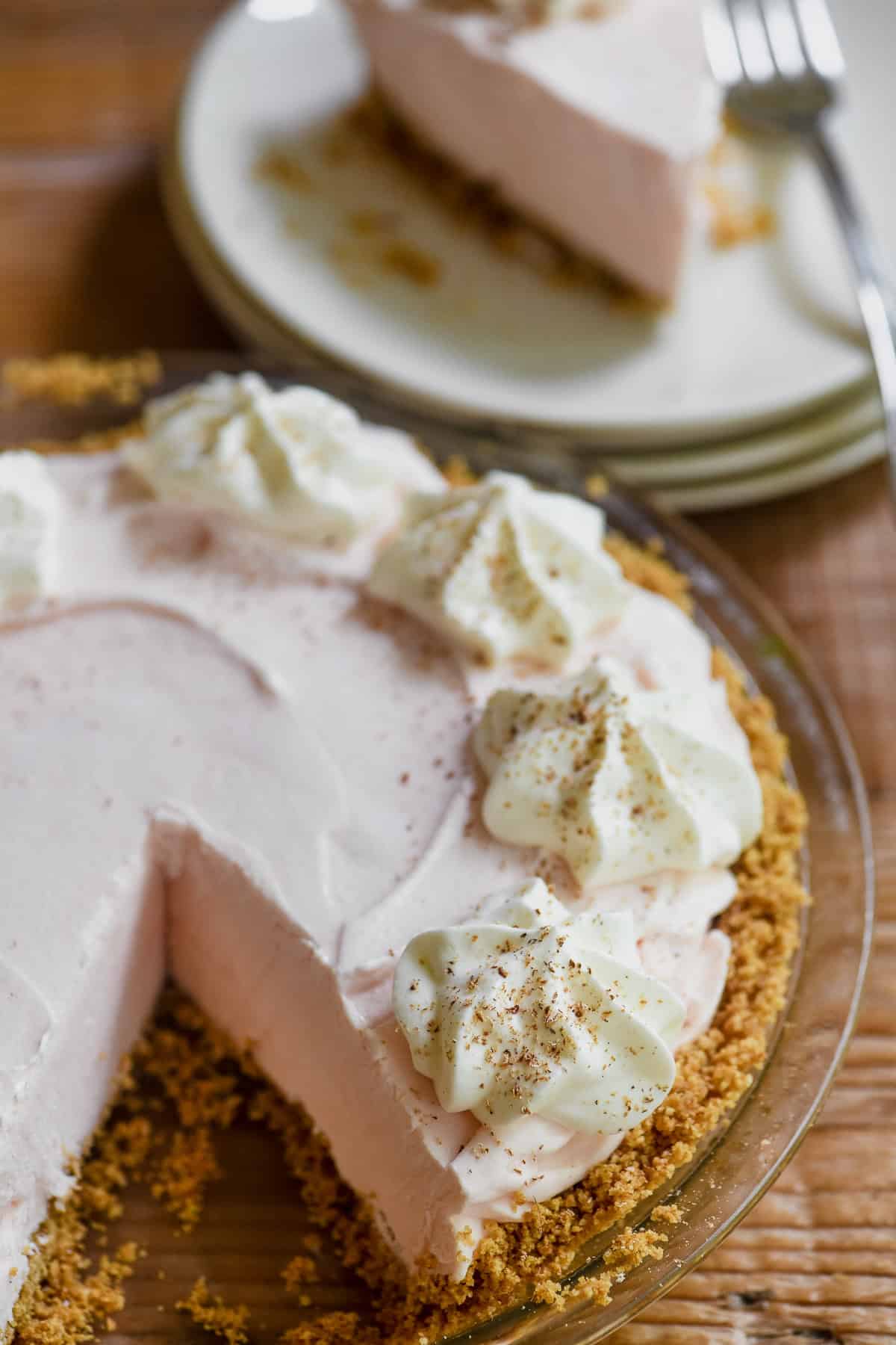 A frozen Pink Squirrel pie topped with whipped cream and nutmeg, with piece removed.