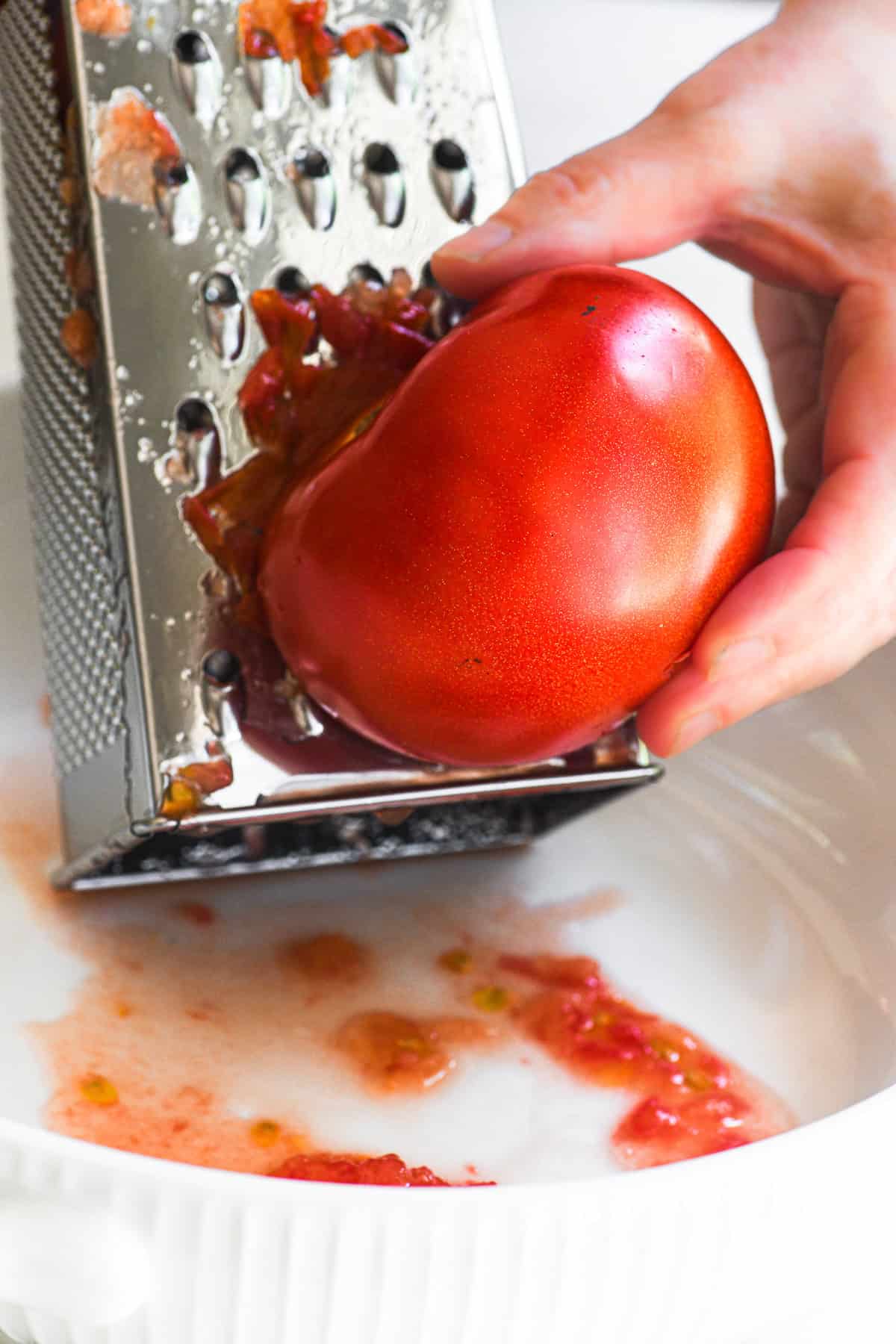 Grating a tomato on a box grater for no bake Mediterranean pasta sauce.