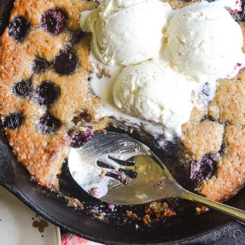 cherry almond skillet cake in a cast iron skillet, topped with vanilla ice cream.