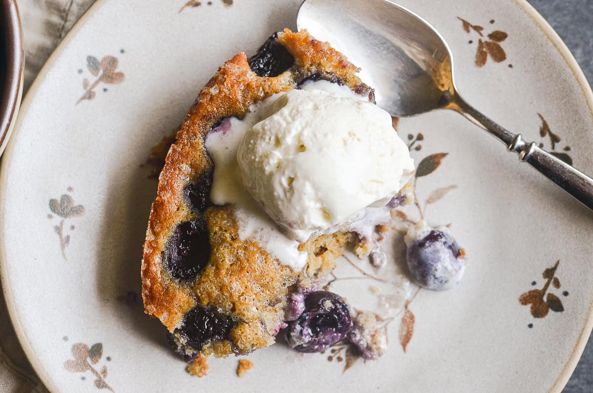 A piece of cherry almond skillet cake with vanilla ice cream on a plate.