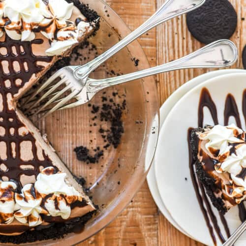frozen mudslide pie. drizzled with chocolate syrup and topped with whipped cream, with a slice on a plate.