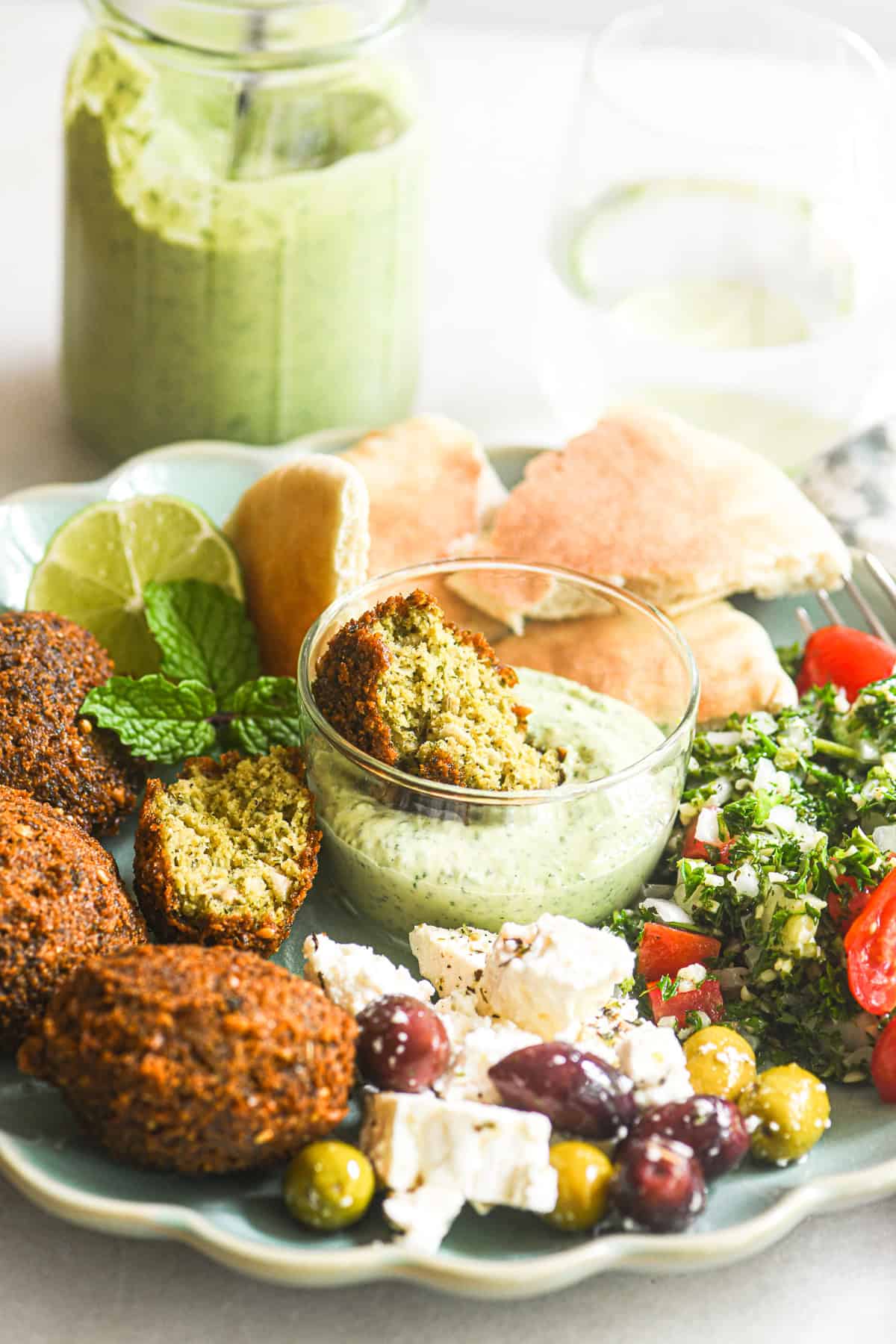 Dipping falafel into a small bowl of green tahini sauce.