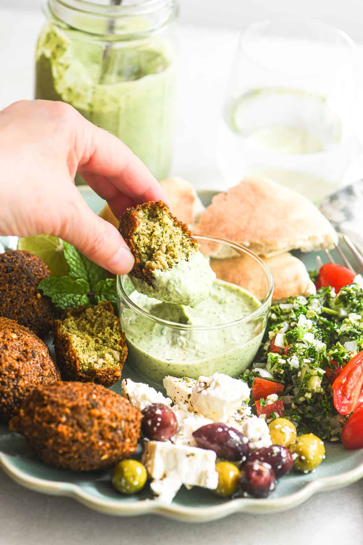 Dipping falafel into a small bowl of green tahini.