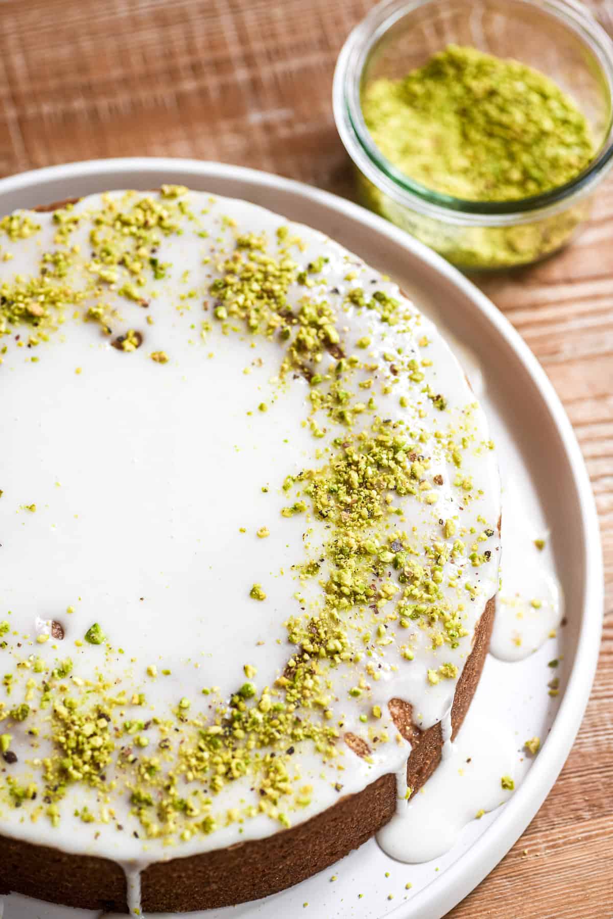 Lemon pistachio snack cake, glazed, with small bowl of crushed pistachios.