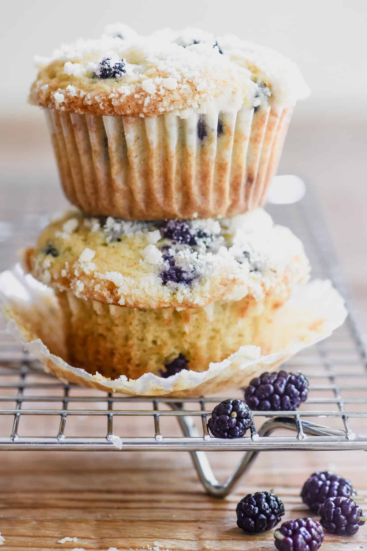 A stack of 2 mulberry muffins on a rack, with fresh mulberries.