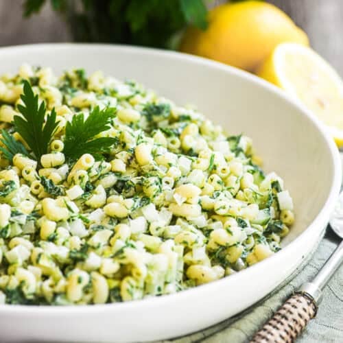 Lemon herb macaroni salad in a white serving bowl topped with parsley and lemon.