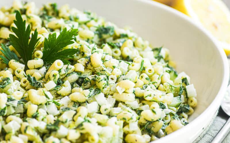 Lemon herb macaroni salad in a white serving bowl topped with parsley and lemon.