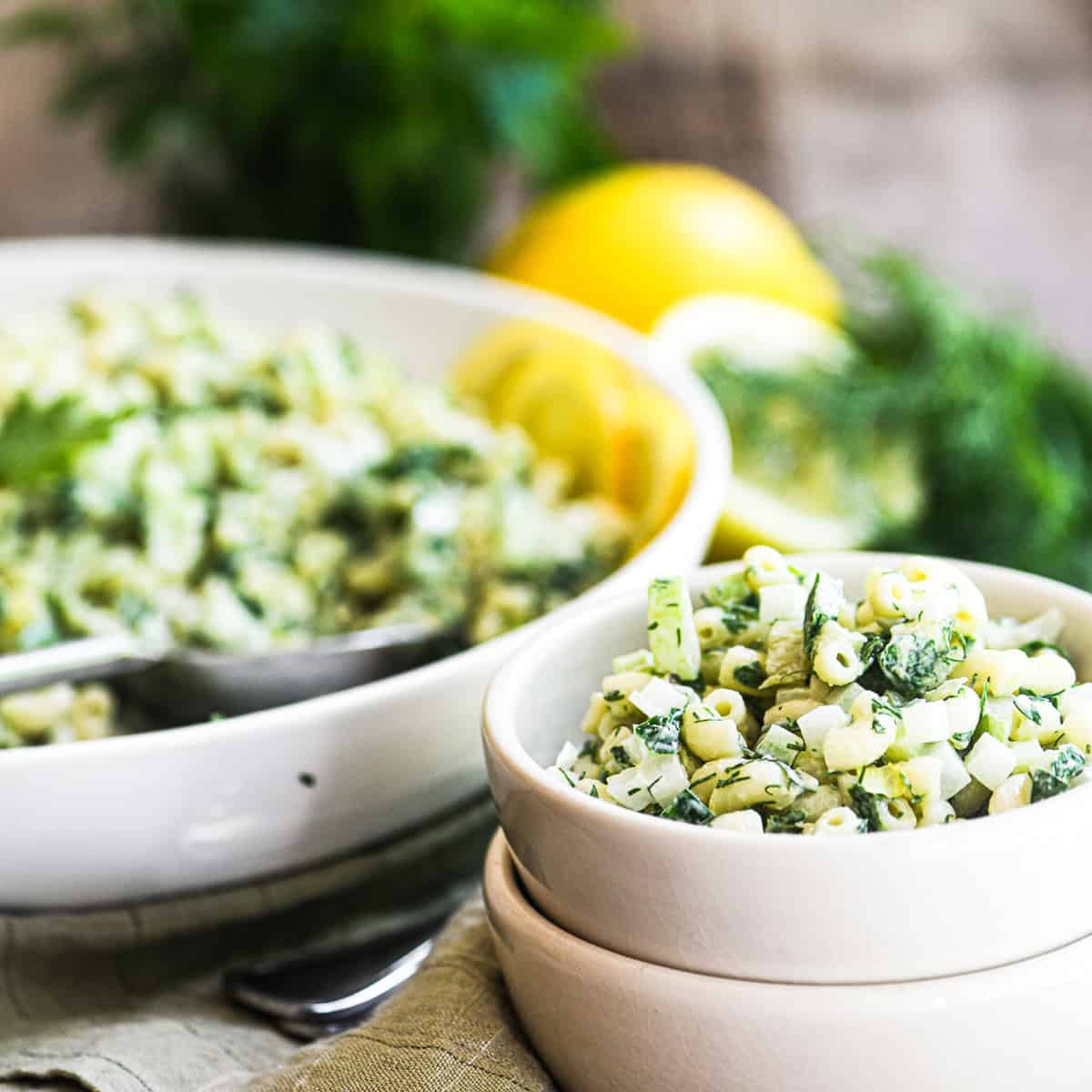 lemon herb macaroni salad in white bowls, with herbs and lemons.