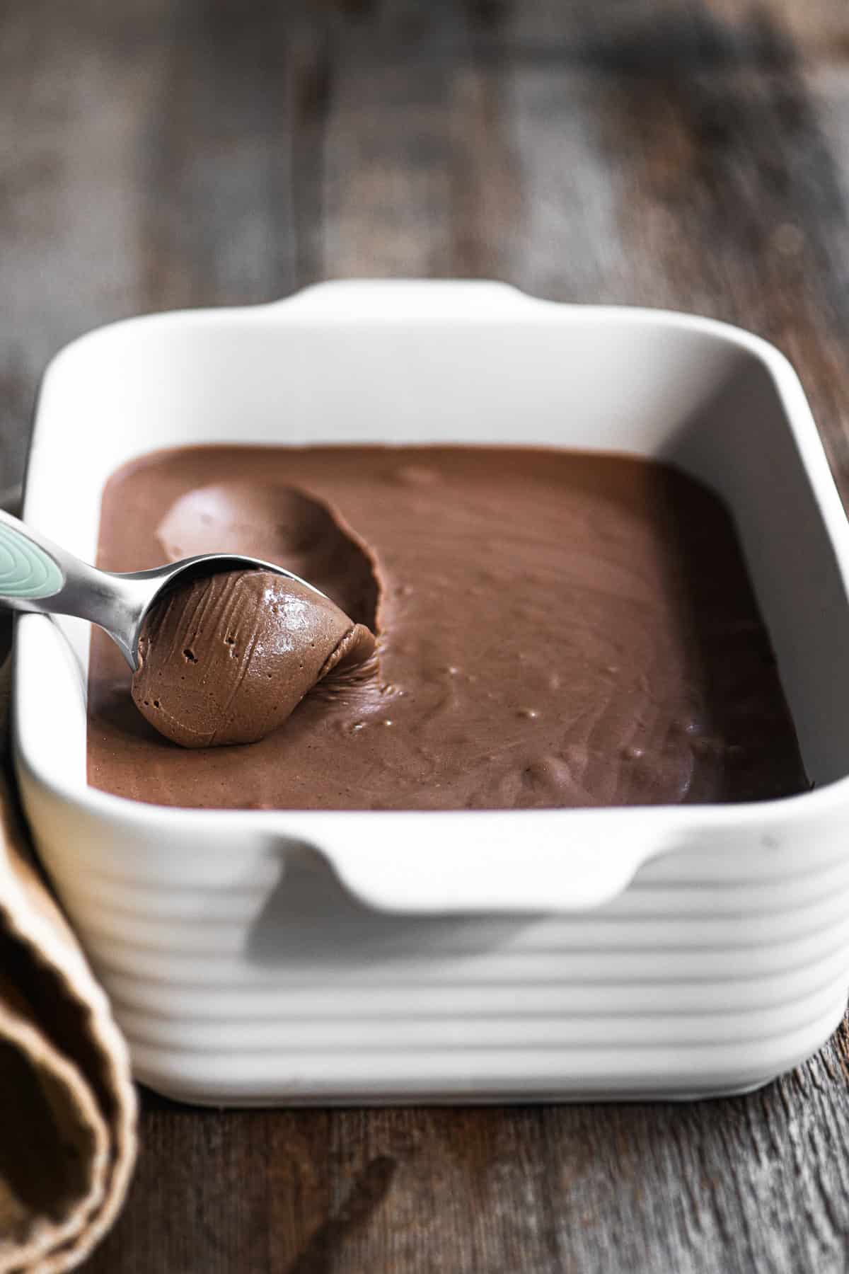 Scooping no-churn Nutella ice cream out of a pan.