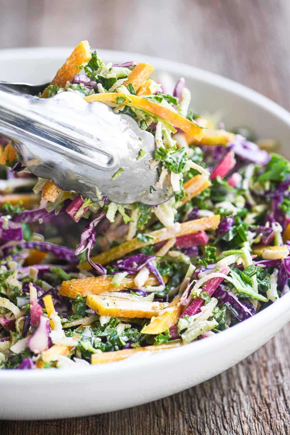 A bowl of power slaw with tongs serving it.