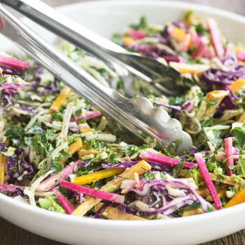 A bowl of colorful power slaw with metal tongs.