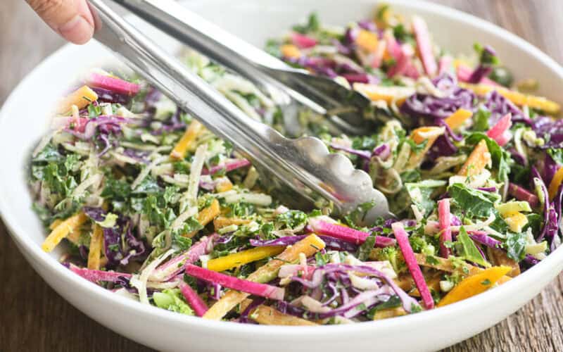 A bowl of colorful power slaw with metal tongs.
