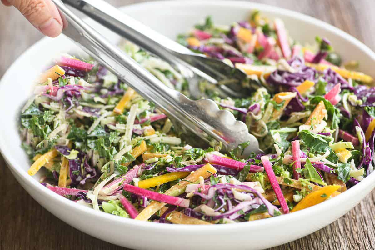 A bowl of colorful power slaw with metal tongs.